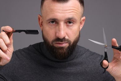 Photo of Bearded man holding blade and scissors on grey background