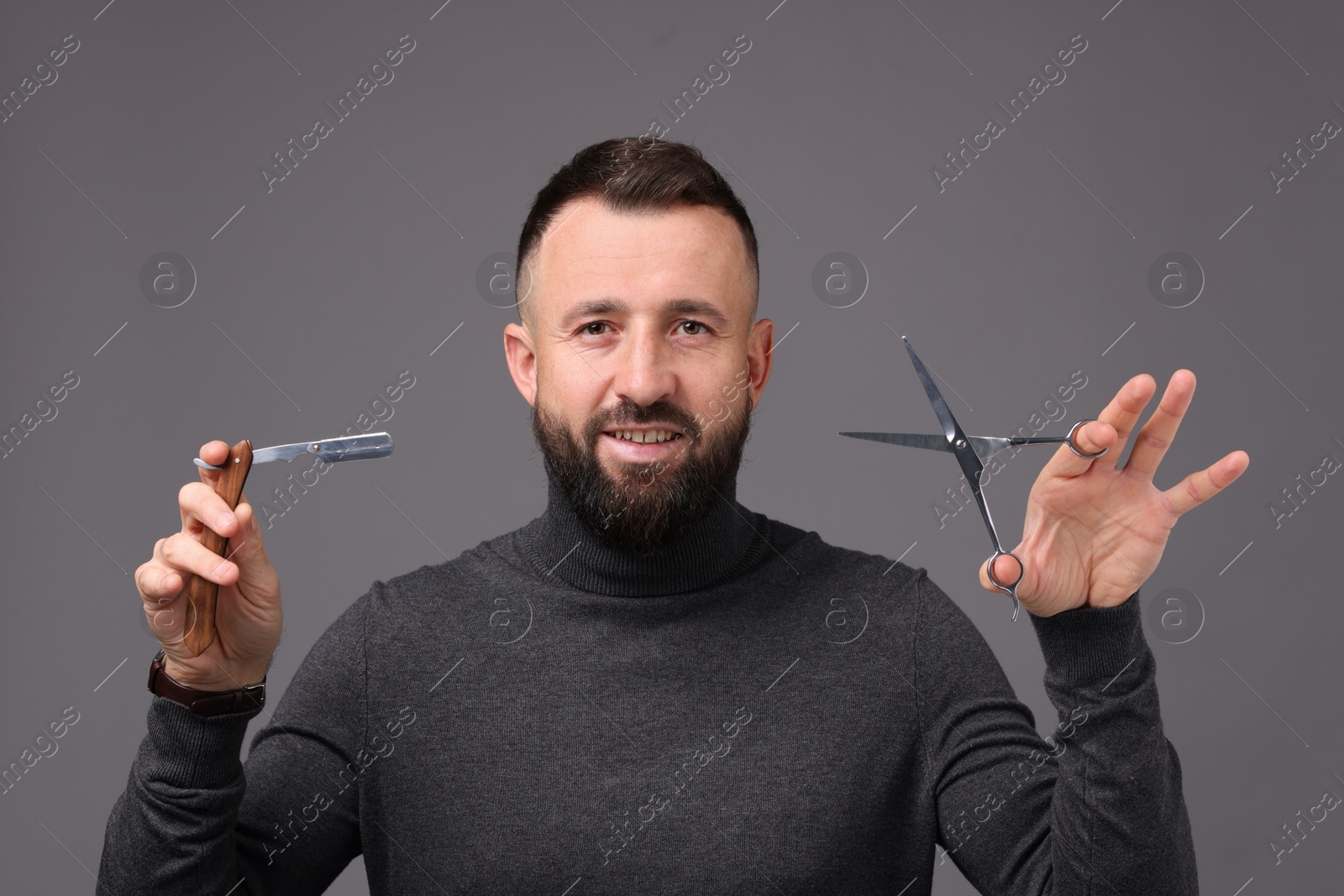 Photo of Bearded man holding blade and scissors on grey background