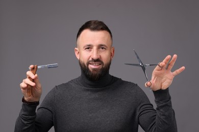 Photo of Bearded man holding blade and scissors on grey background