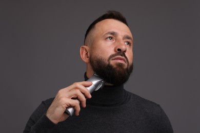 Photo of Handsome man trimming beard on grey background