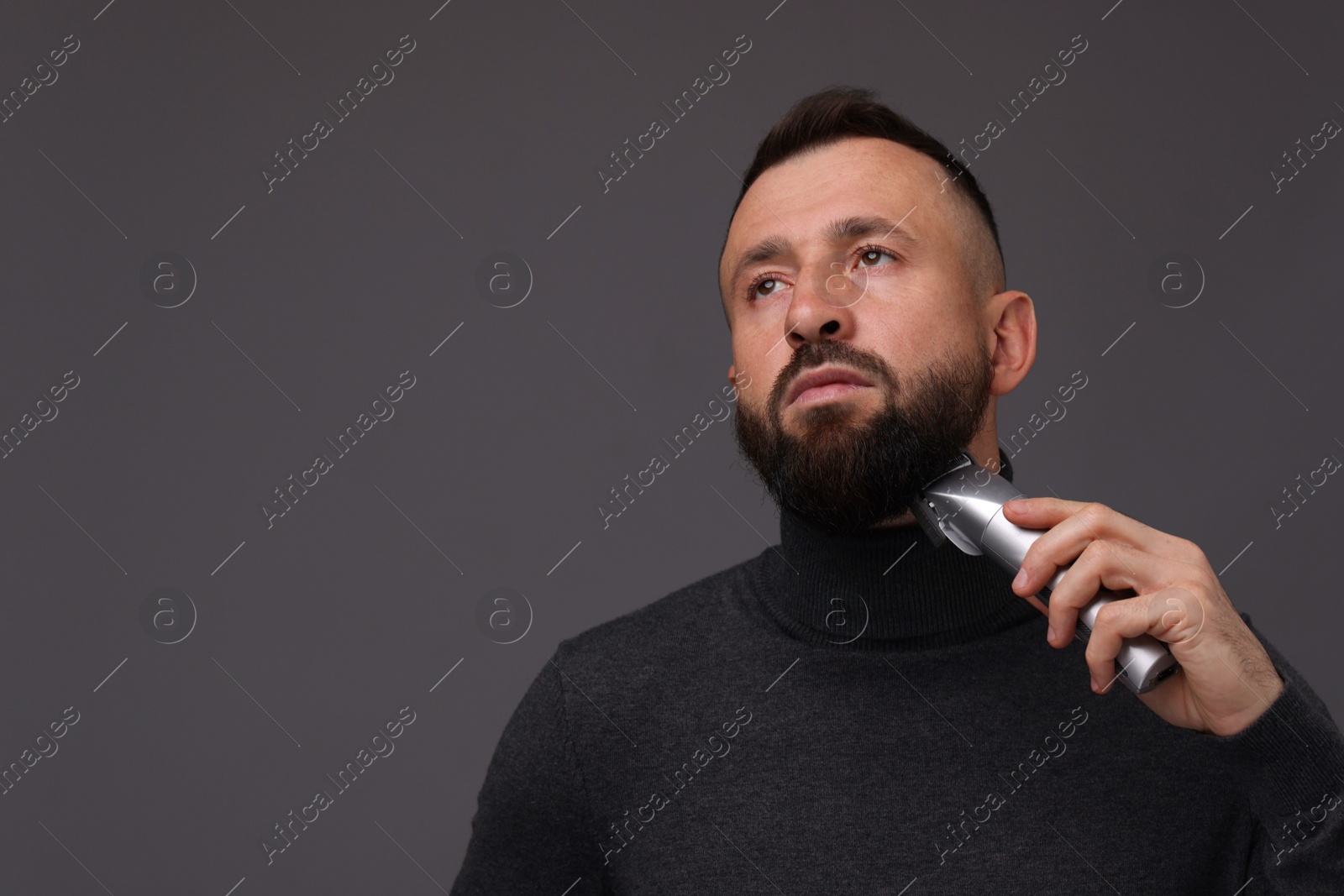 Photo of Handsome man trimming beard on grey background, space for text