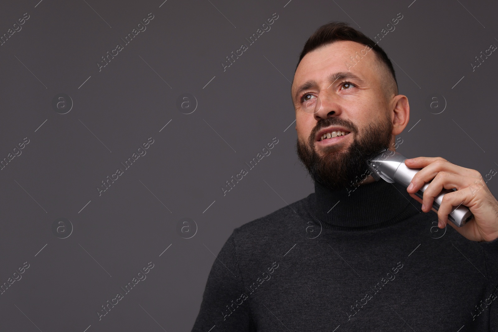 Photo of Handsome man trimming beard on grey background, space for text