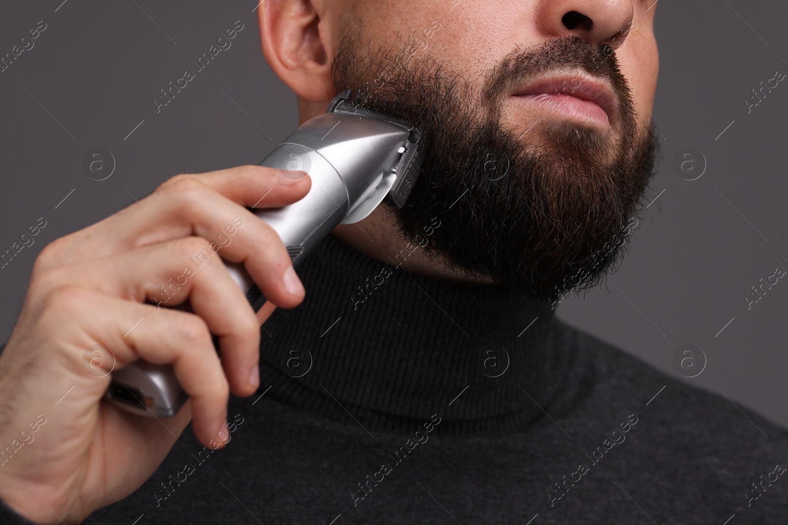 Photo of Man trimming beard on grey background, closeup