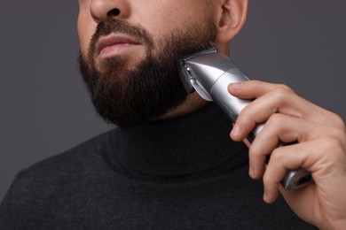 Photo of Man trimming beard on grey background, closeup