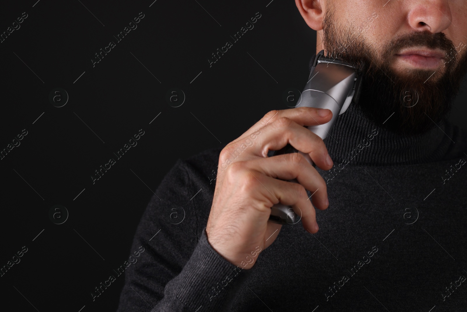 Photo of Man trimming beard on black background, closeup. Space for text