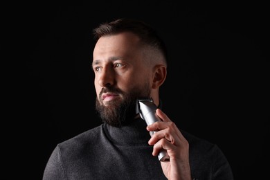 Photo of Handsome man trimming beard on black background