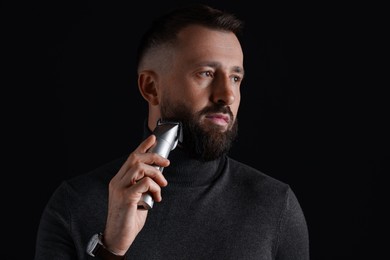 Photo of Handsome man trimming beard on black background