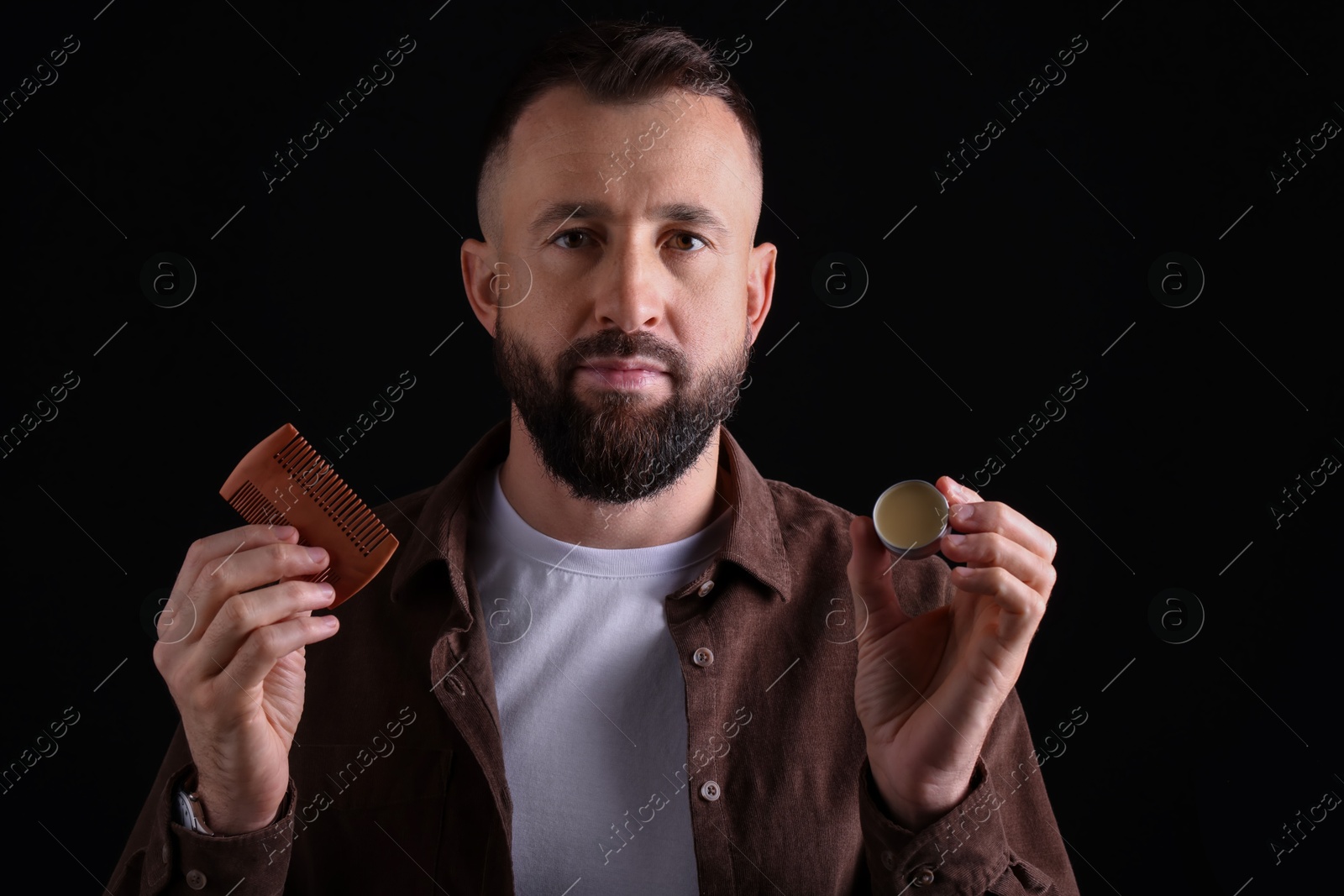 Photo of Handsome bearded man with comb and balm on black background