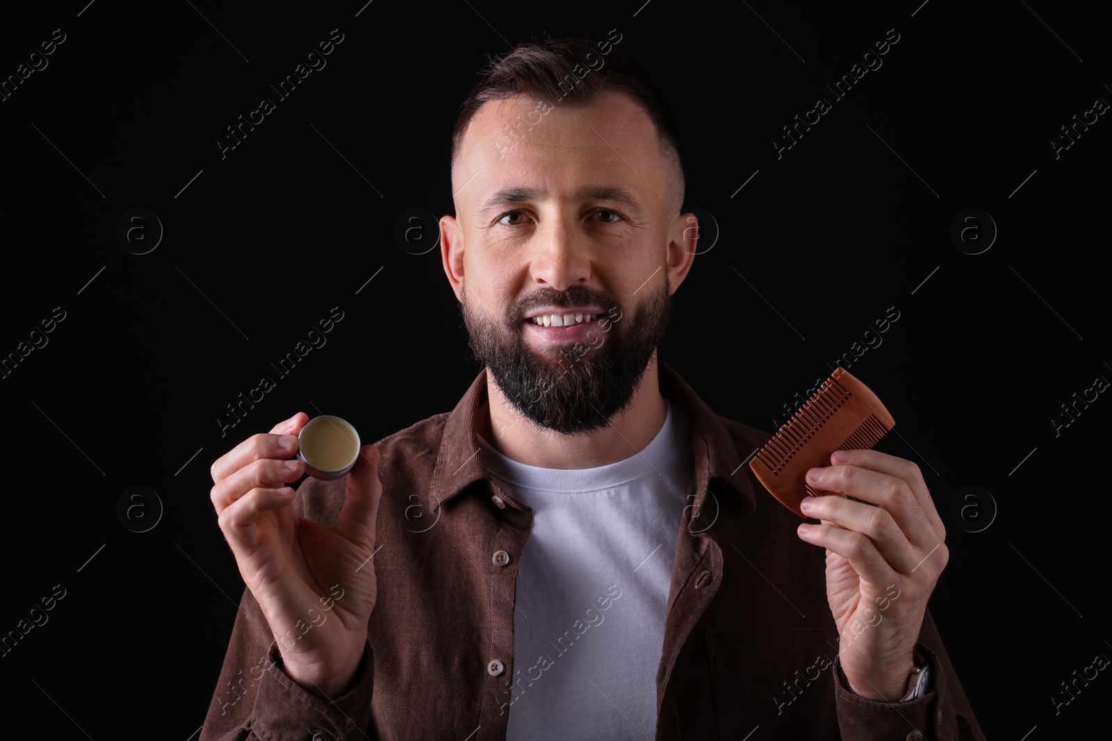 Photo of Handsome bearded man with comb and balm on black background