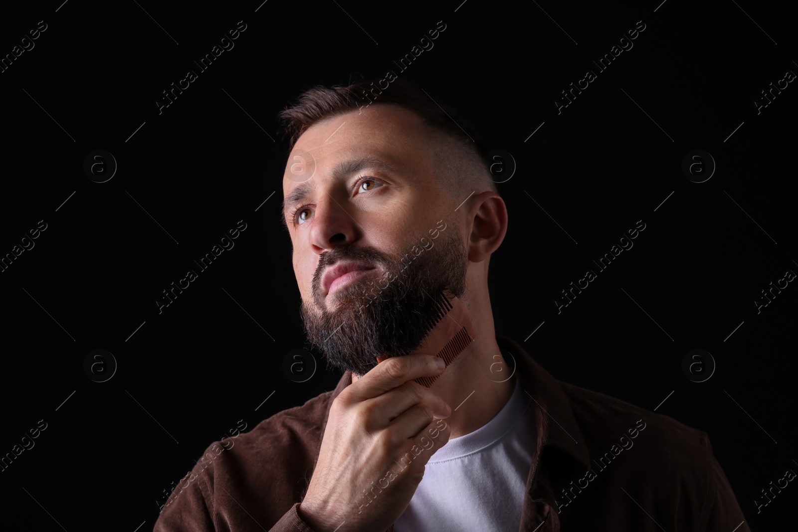 Photo of Handsome man combing beard on black background