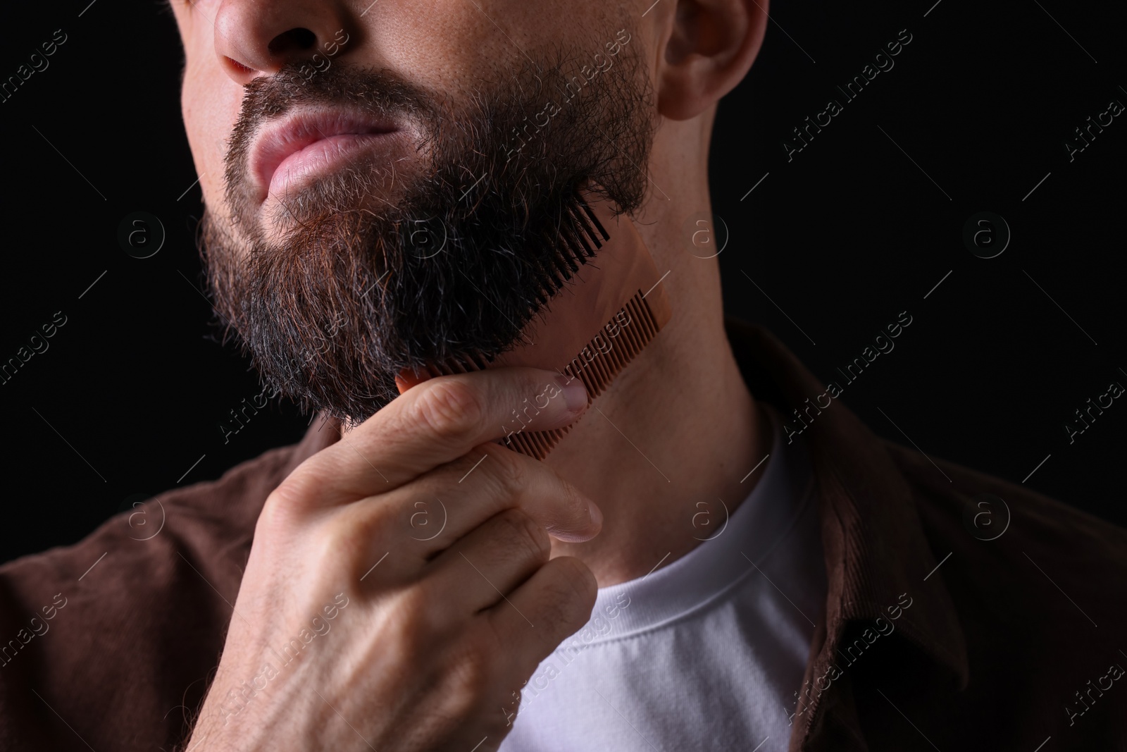 Photo of Man combing beard on black background, closeup