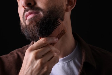 Photo of Man combing beard on black background, closeup