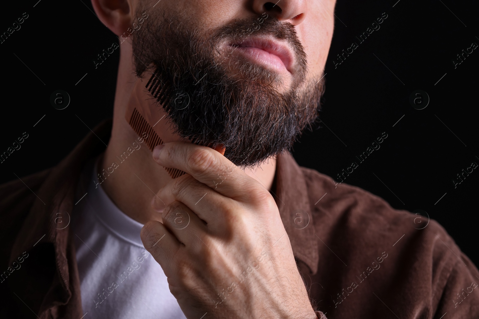 Photo of Man combing beard on black background, closeup