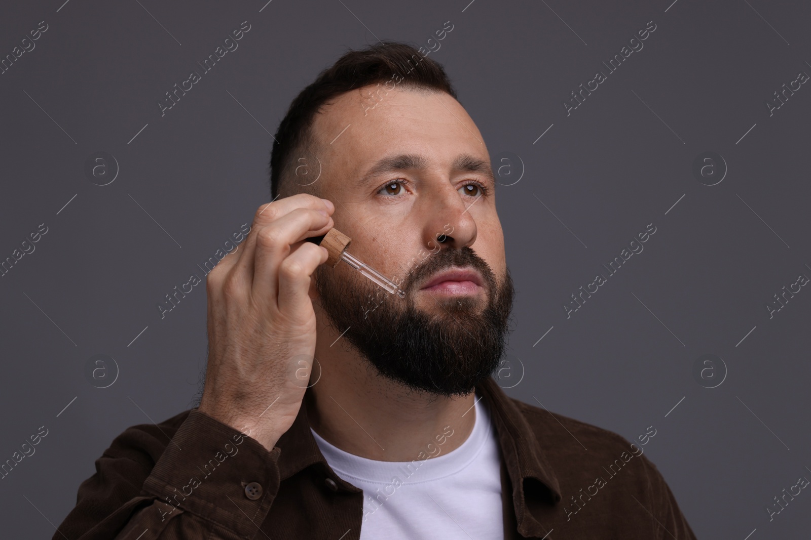 Photo of Man applying serum onto his beard on grey background