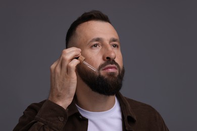 Photo of Man applying serum onto his beard on grey background