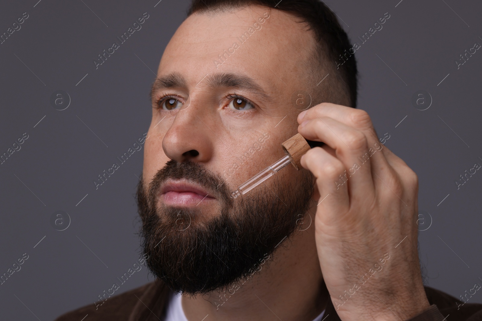 Photo of Man applying serum onto his beard on grey background