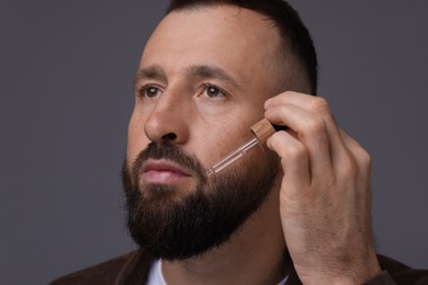 Photo of Man applying serum onto his beard on grey background