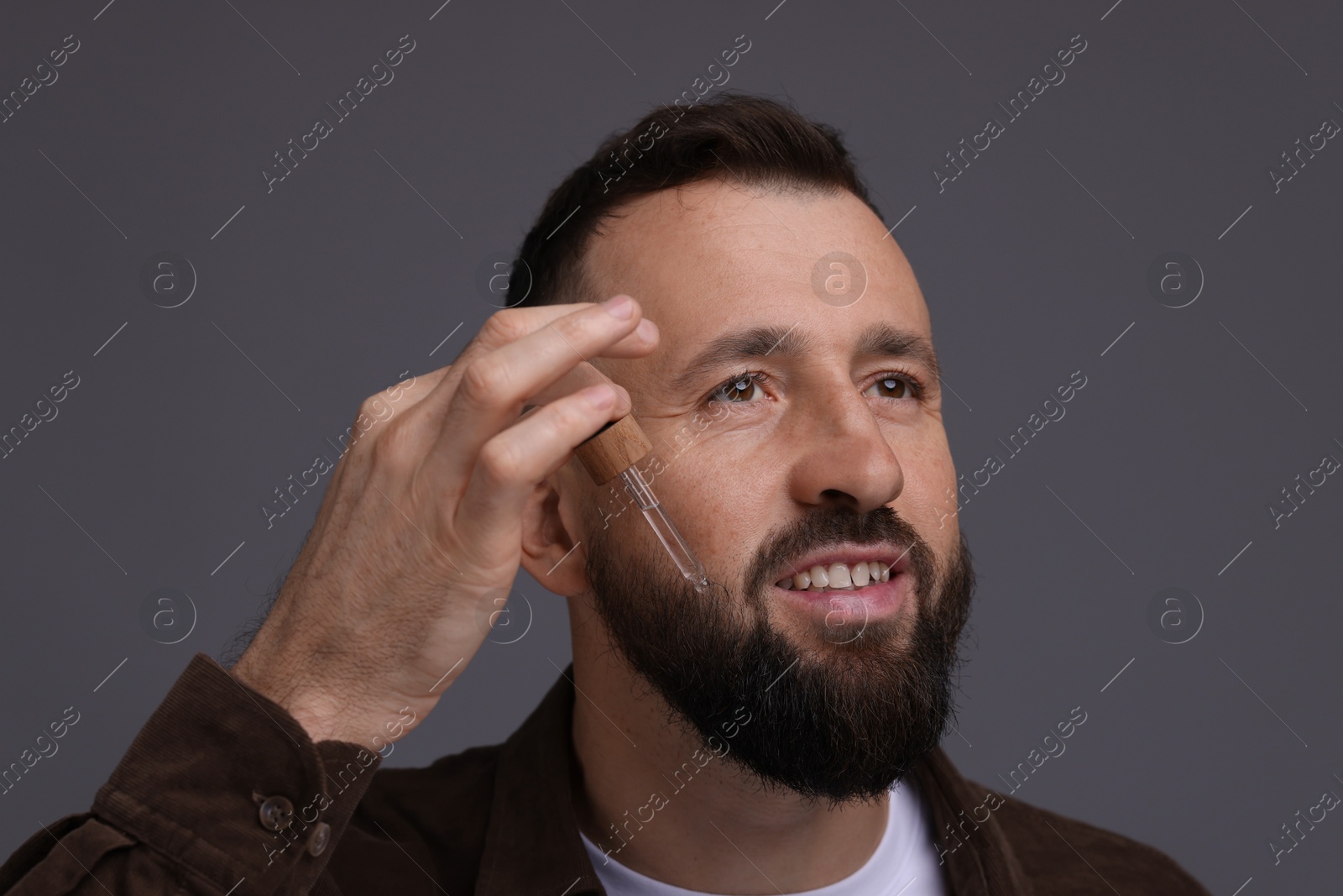 Photo of Man applying serum onto his beard on grey background