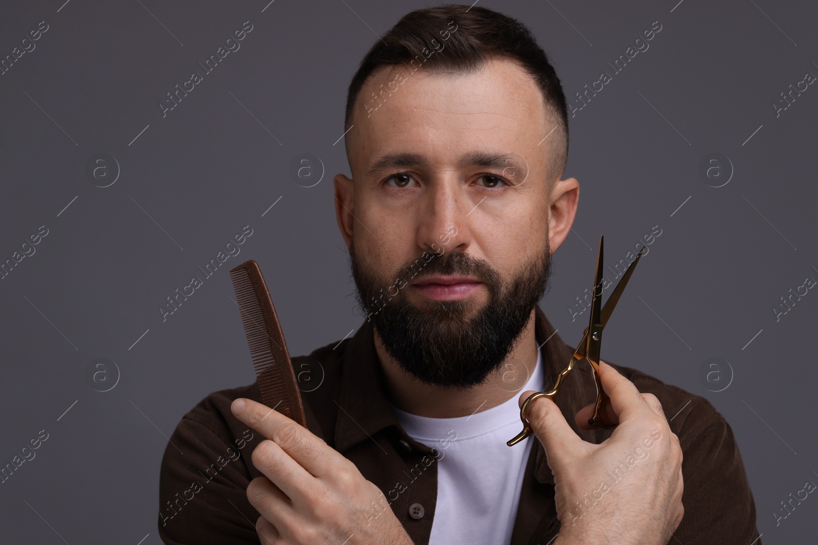 Photo of Bearded man holding comb and scissors on grey background