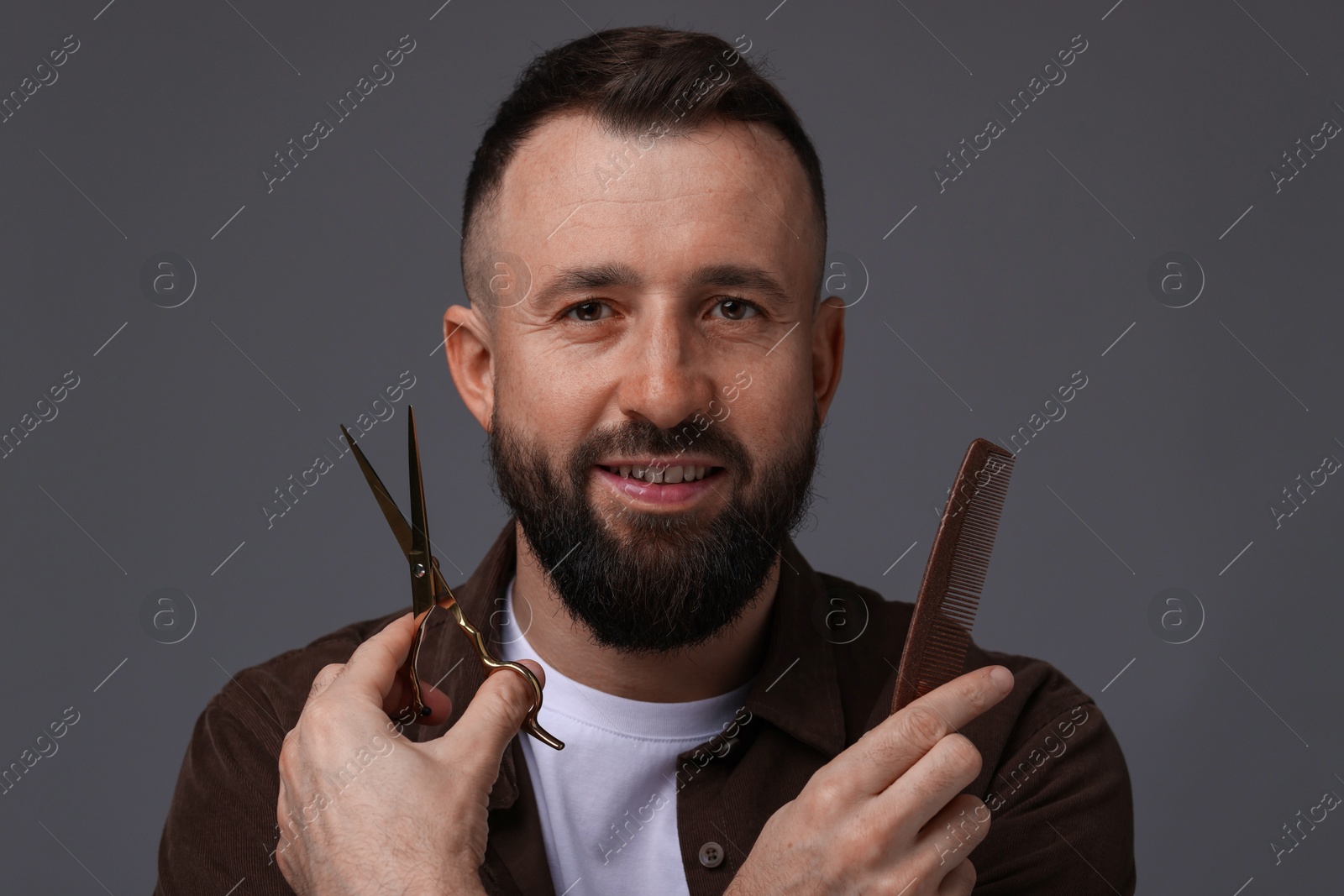 Photo of Bearded man holding comb and scissors on grey background