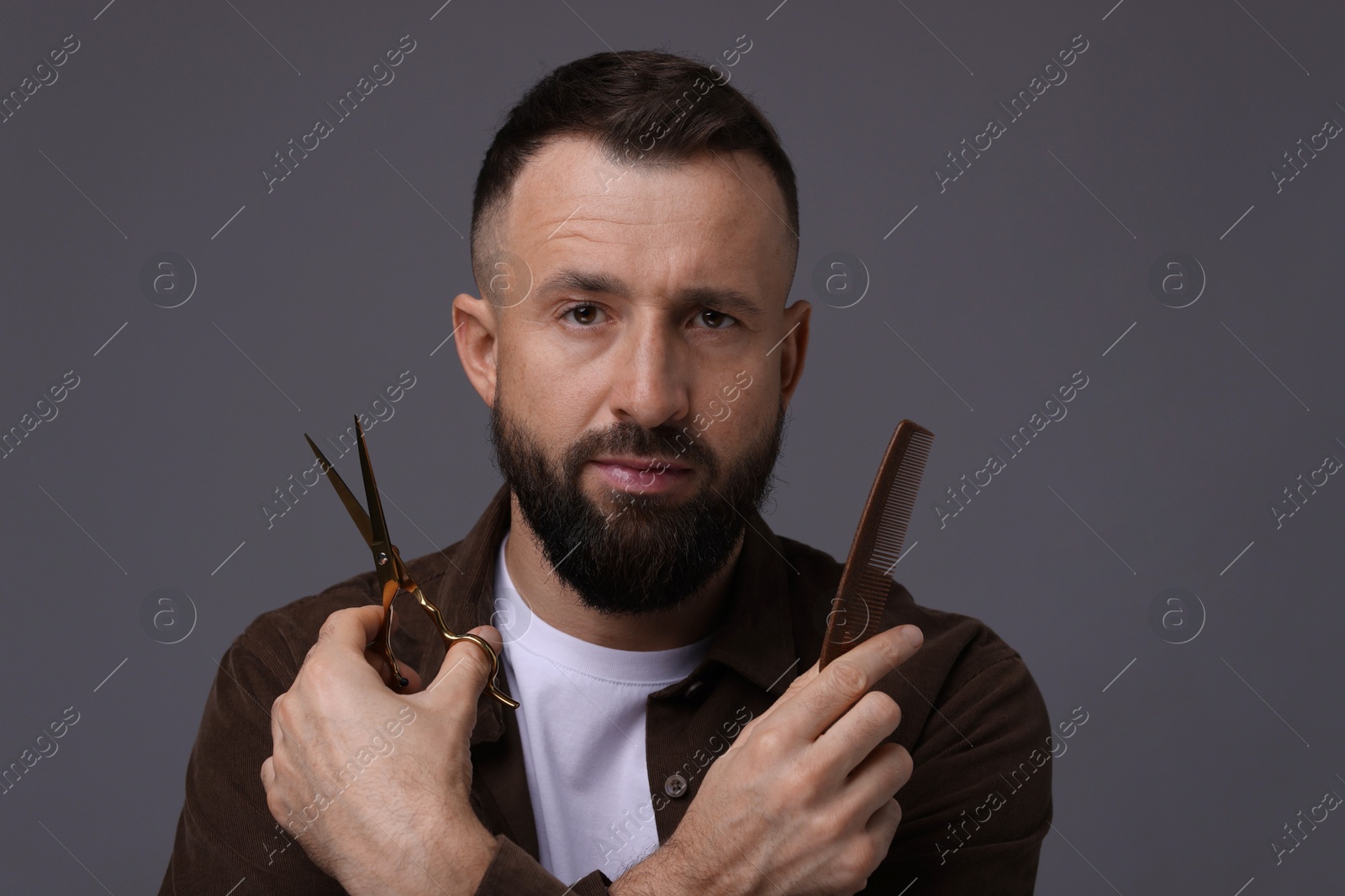 Photo of Bearded man holding comb and scissors on grey background