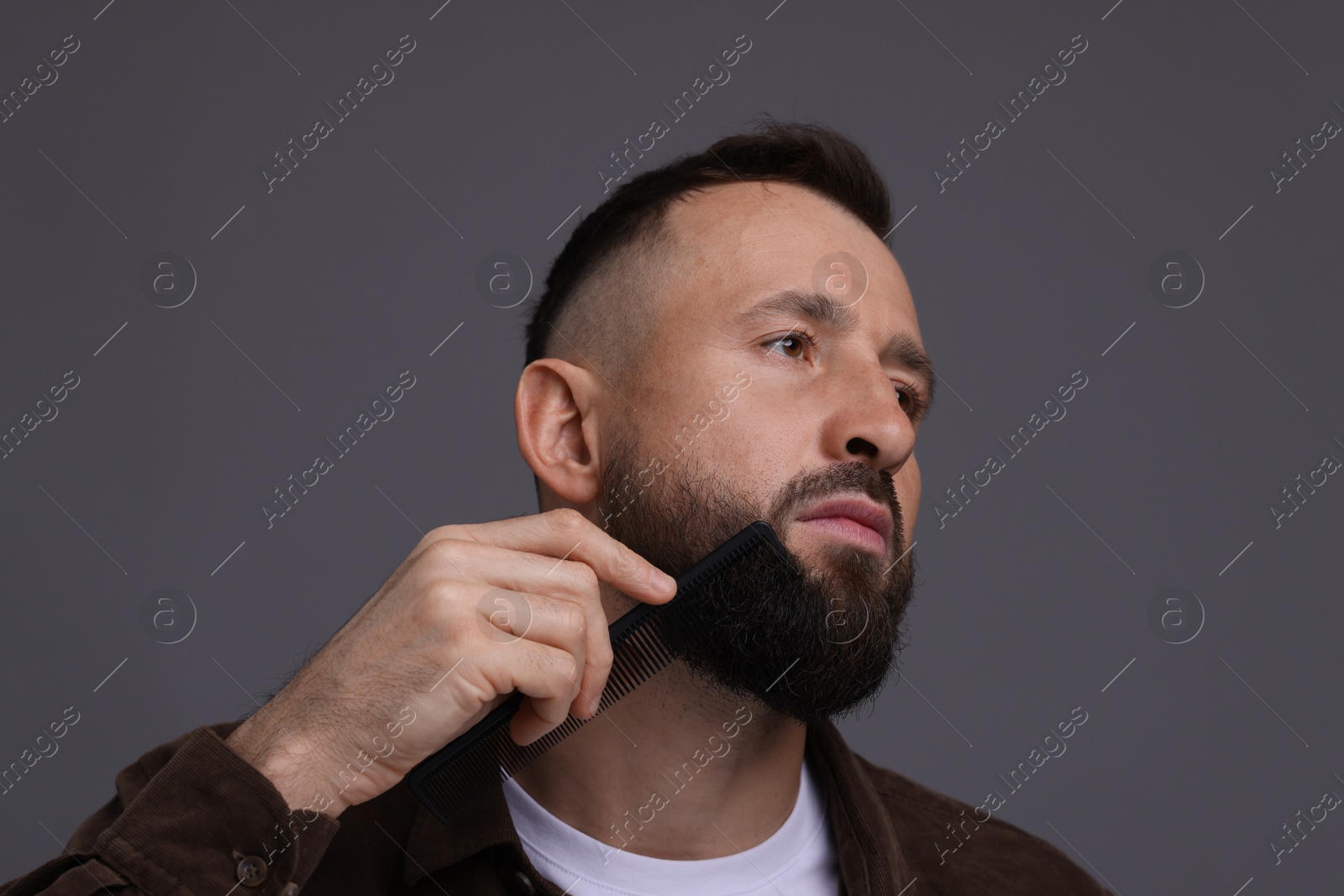 Photo of Handsome man combing beard on grey background