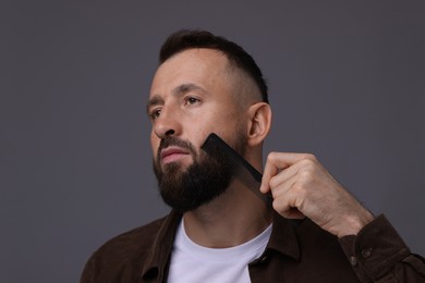 Photo of Handsome man combing beard on grey background