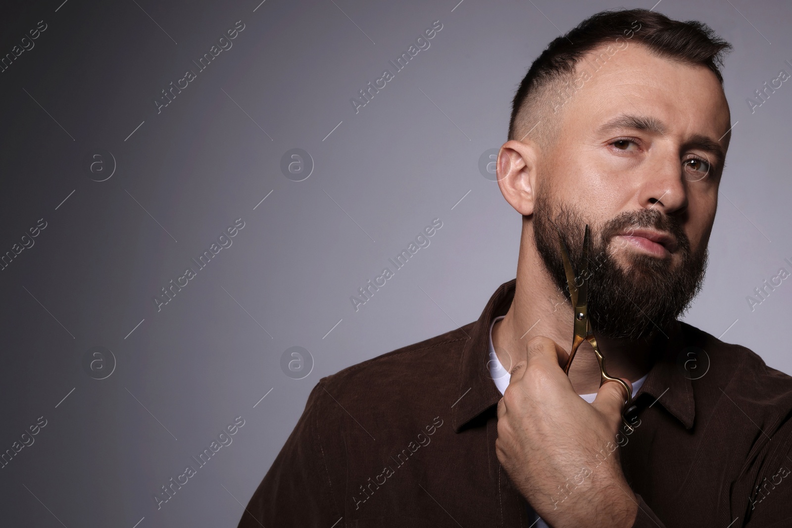 Photo of Man trimming beard with scissors on grey background, space for text