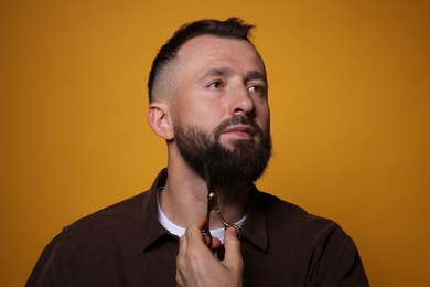 Photo of Man trimming beard with scissors on orange background