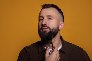 Man trimming beard with scissors on orange background