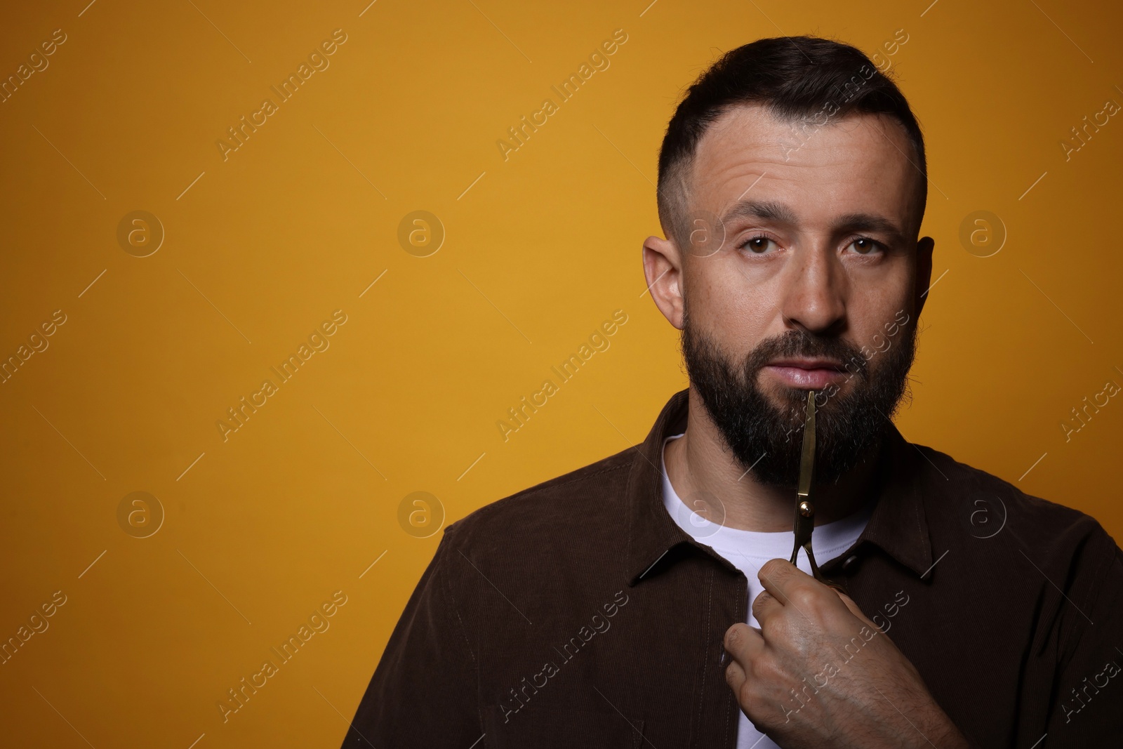 Photo of Bearded man with scissors on orange background, space for text