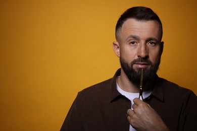 Bearded man with scissors on orange background, space for text