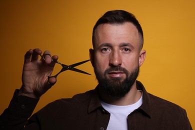 Photo of Bearded man with scissors on orange background