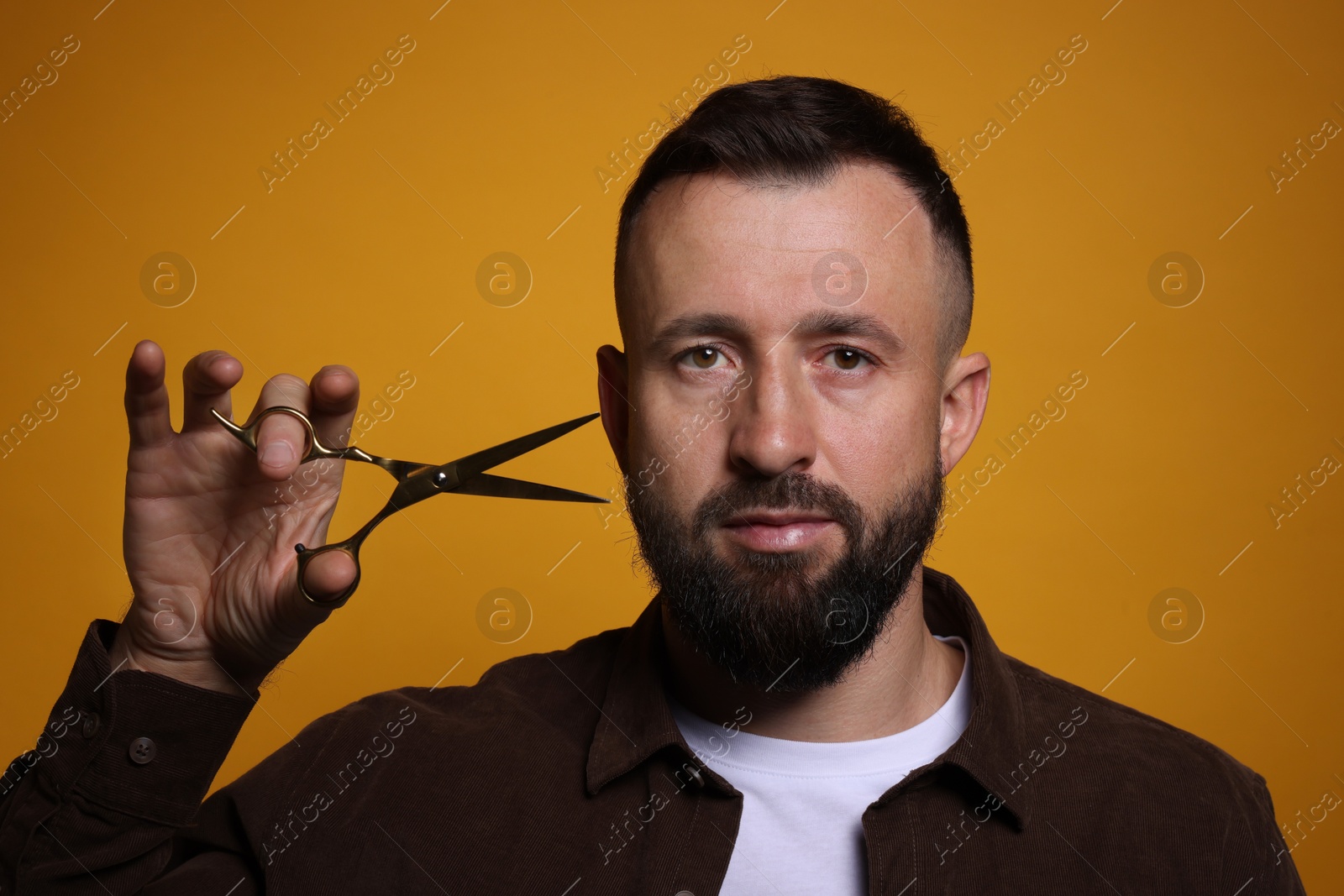 Photo of Bearded man with scissors on orange background