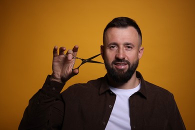 Bearded man with scissors on orange background