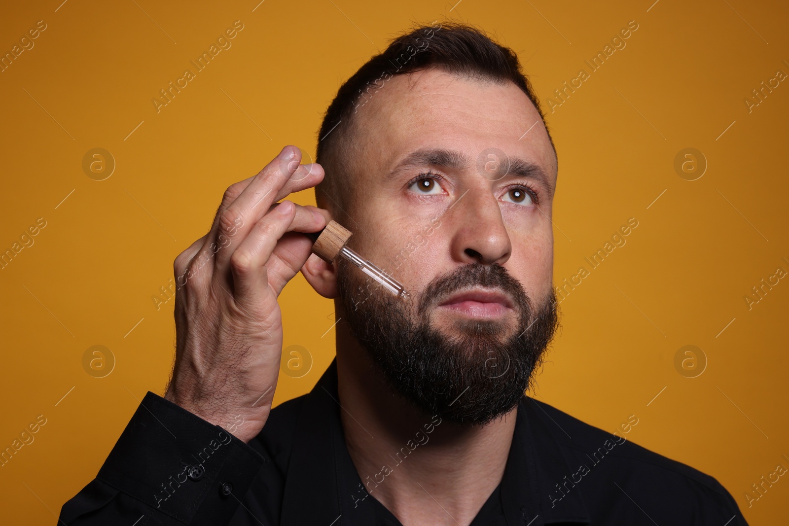 Photo of Man applying serum onto his beard on orange background