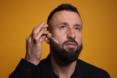 Photo of Man applying serum onto his beard on orange background