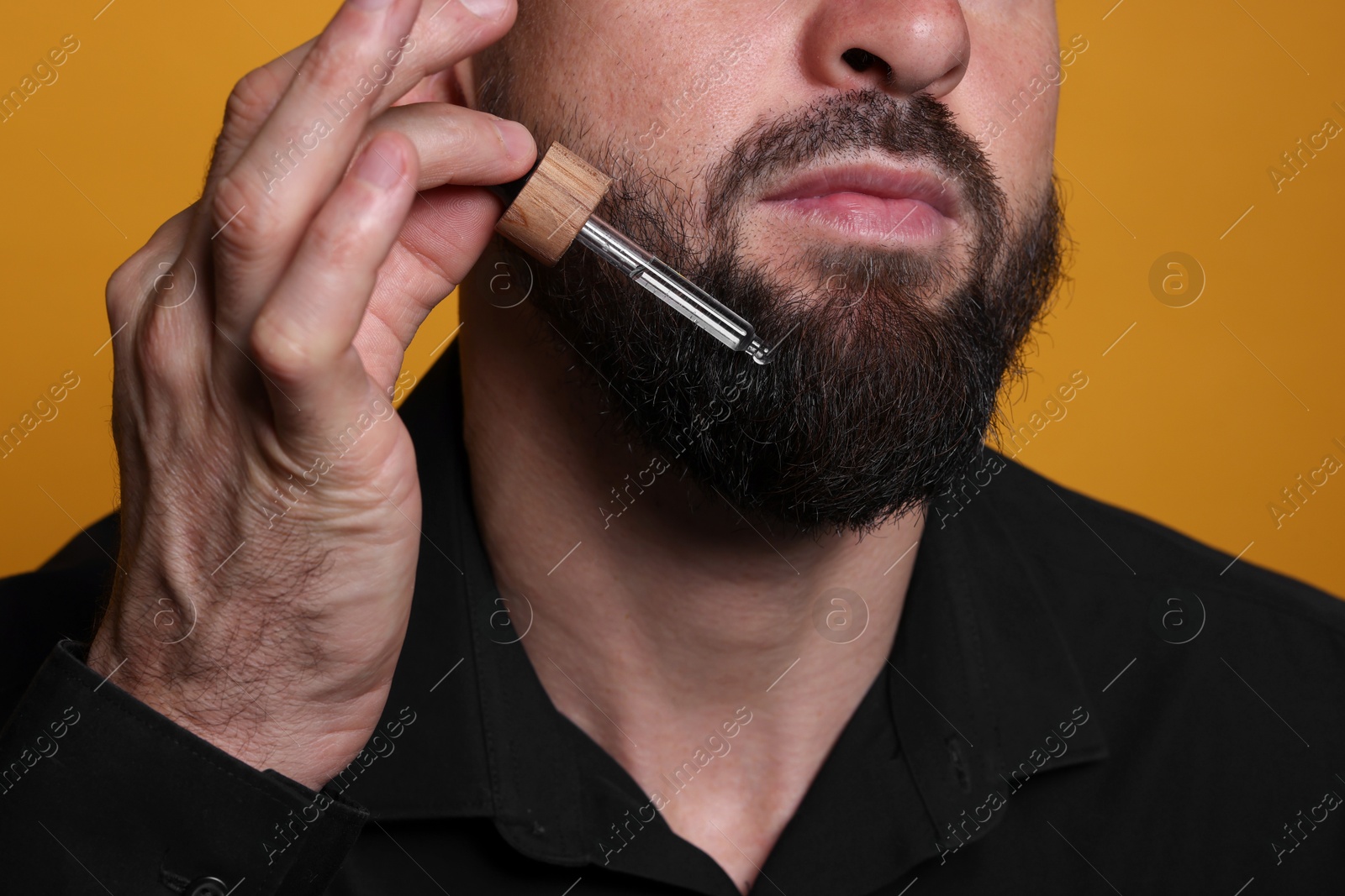 Photo of Man applying serum onto his beard on orange background, closeup