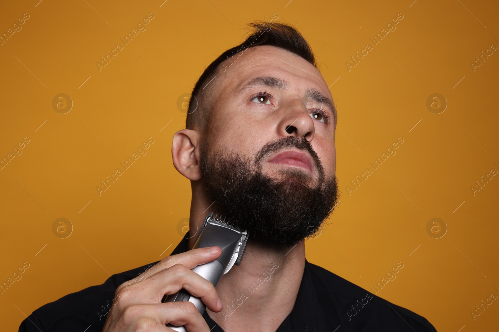 Photo of Handsome man trimming beard on orange background