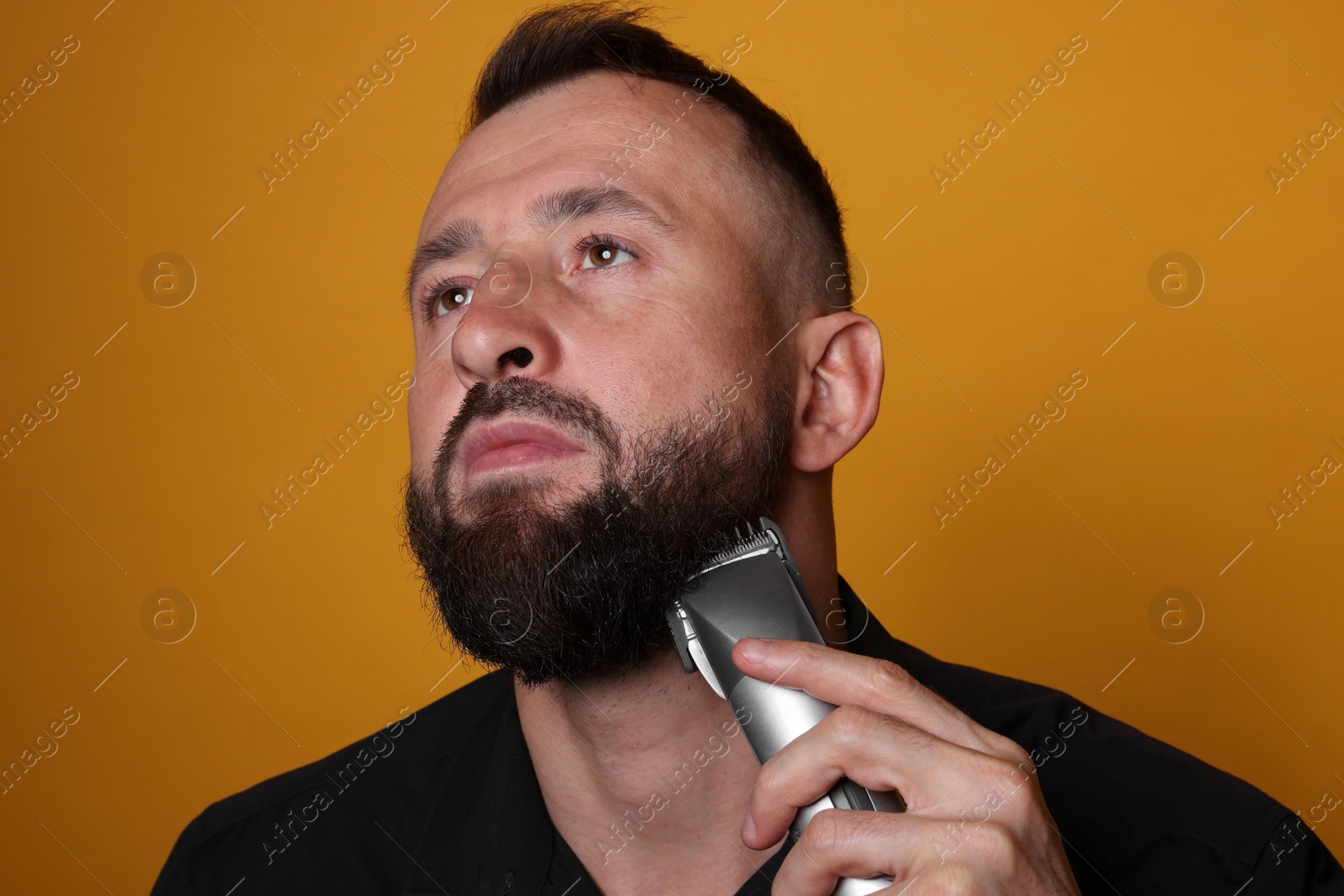 Photo of Handsome man trimming beard on orange background