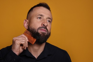 Handsome man combing beard on orange background, space for text