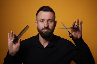 Photo of Bearded man holding comb and scissors on orange background