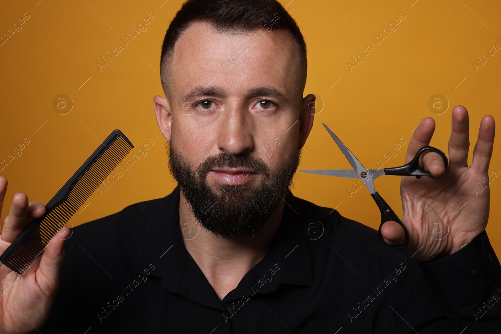 Photo of Bearded man holding comb and scissors on orange background