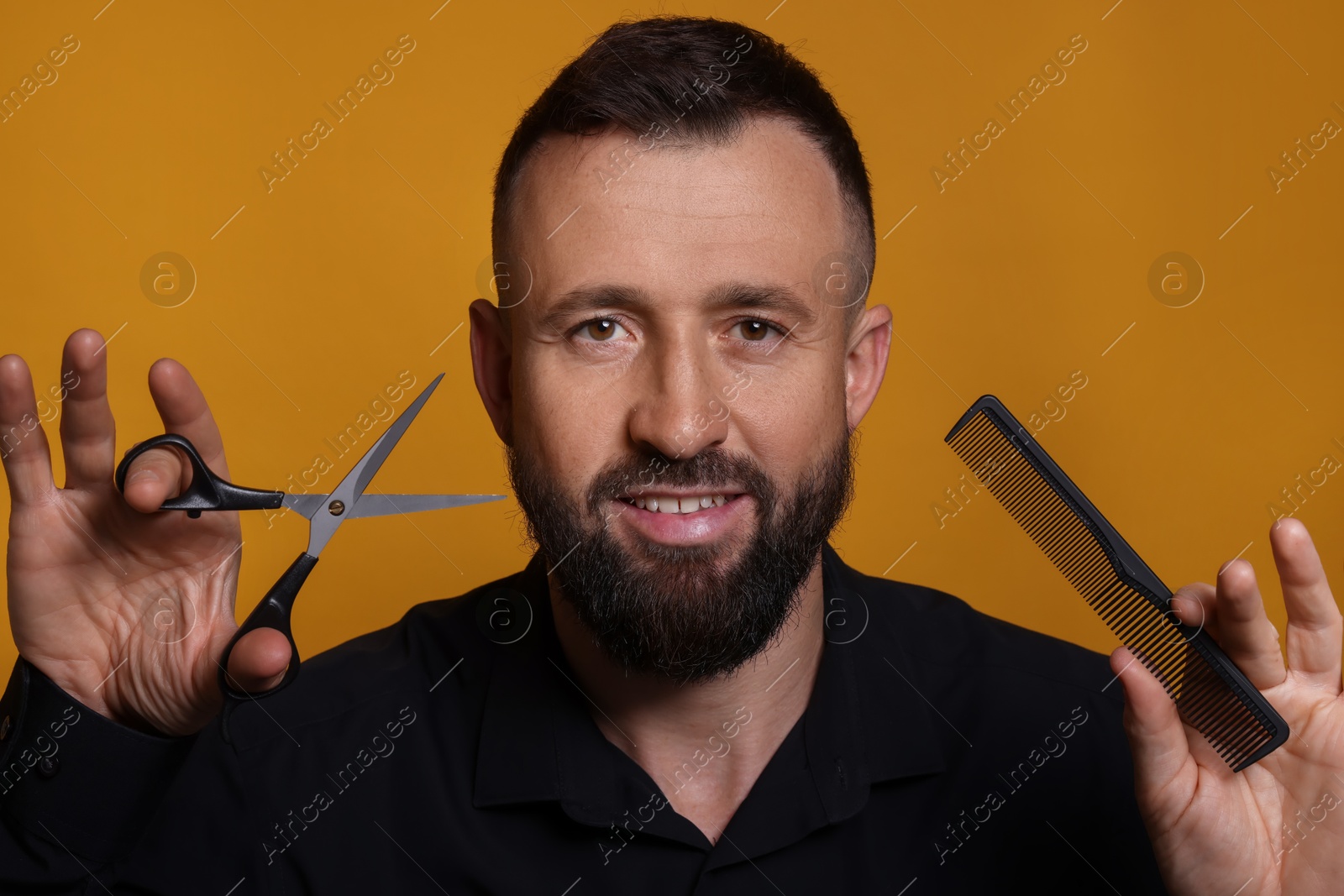 Photo of Bearded man holding comb and scissors on orange background