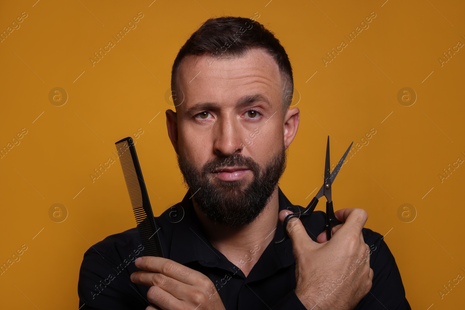 Photo of Bearded man holding comb and scissors on orange background