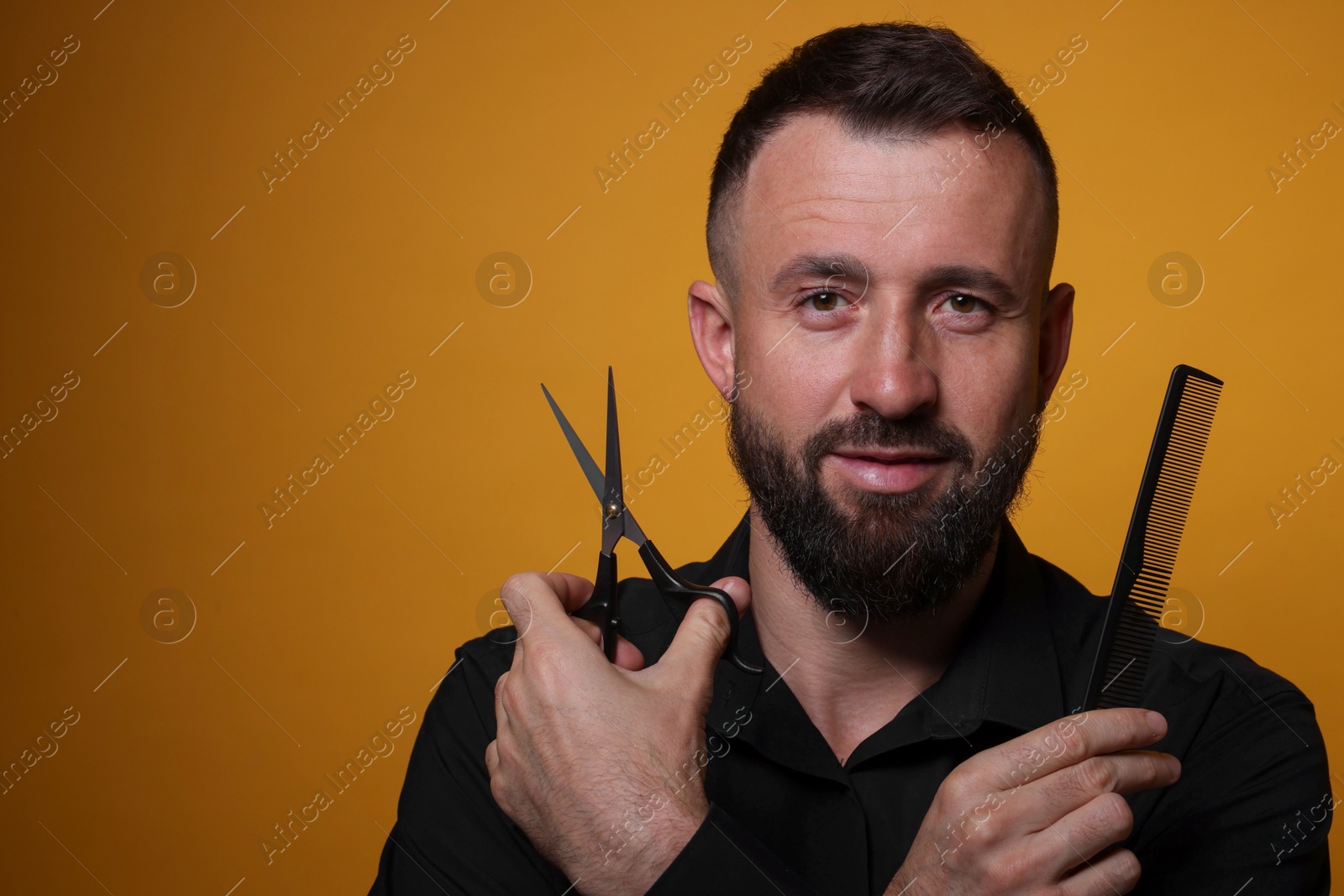 Photo of Bearded man holding comb and scissors on orange background, space for text