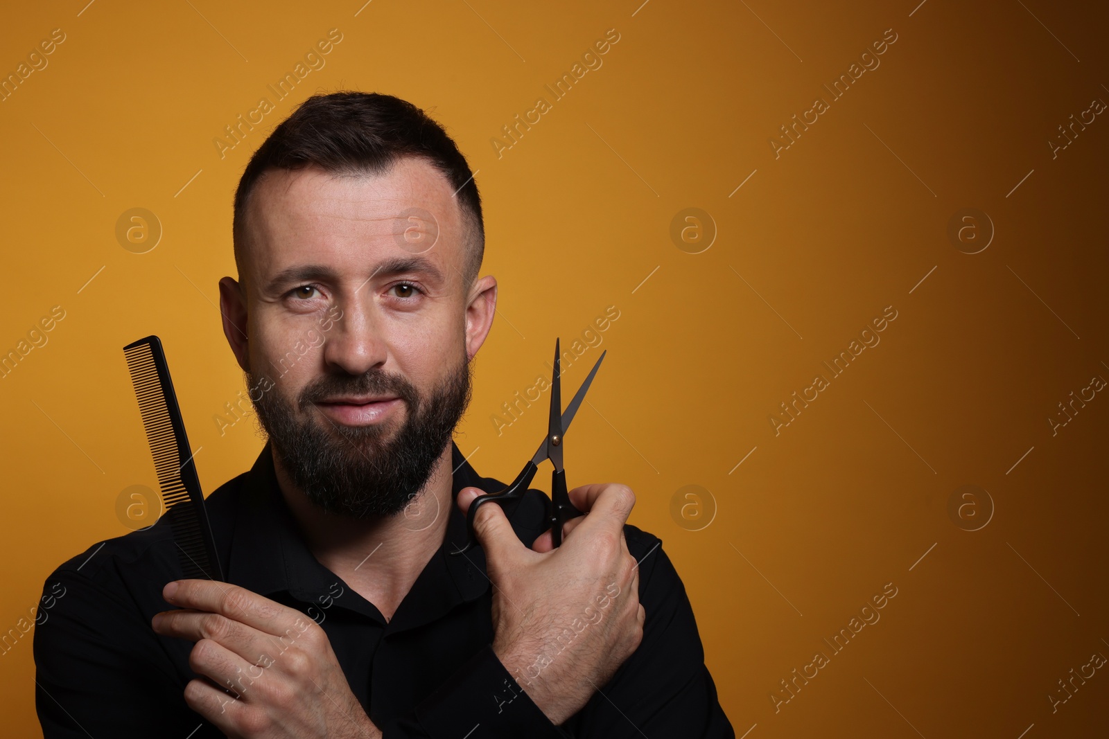 Photo of Bearded man holding comb and scissors on orange background, space for text