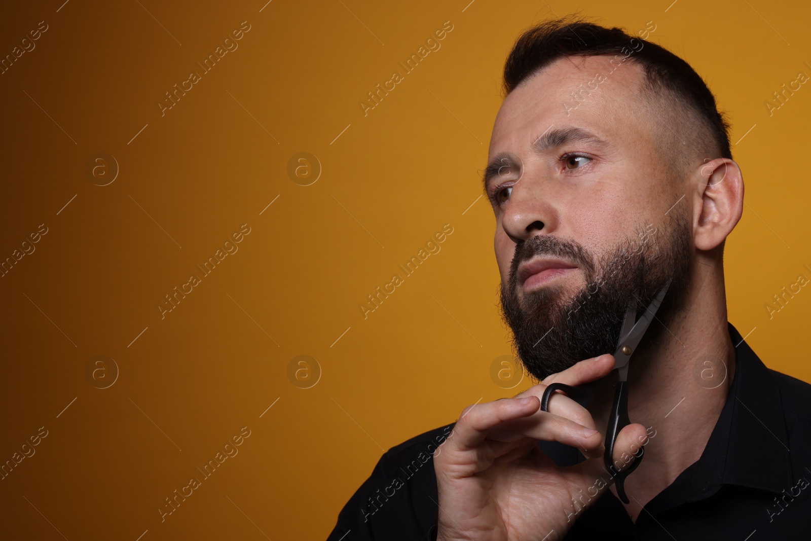 Photo of Man trimming beard with scissors on orange background, space for text