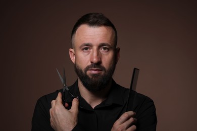 Bearded man holding comb and scissors on brown background