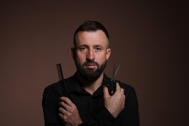 Photo of Bearded man holding comb and scissors on brown background